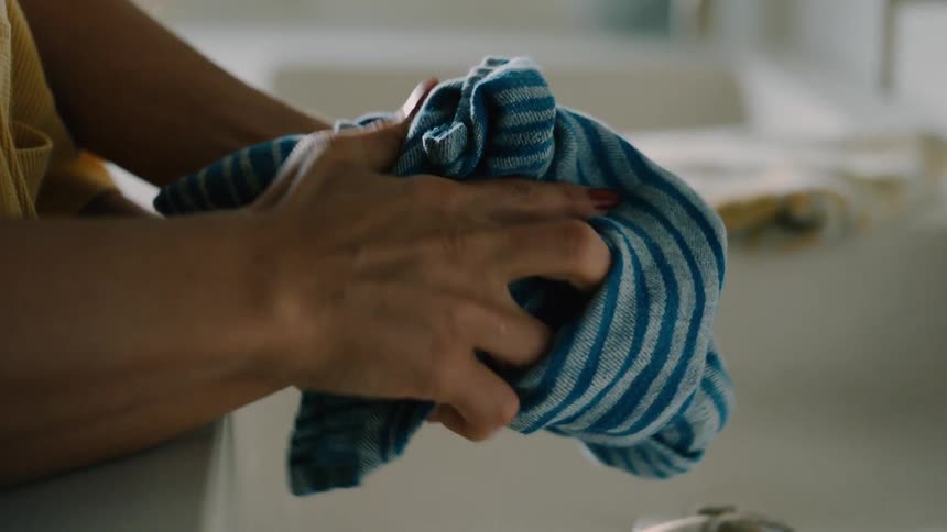An adult uses a cloth to wipe a childs hands at the sink at midday