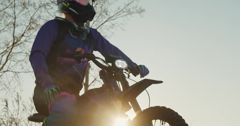 A motocross rider sits still on a dirt bike looking out over a trail at sunset