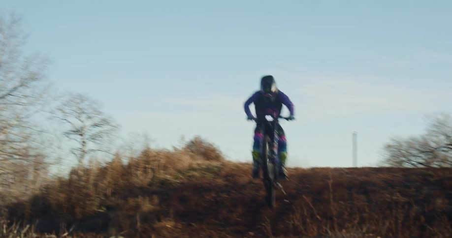 A person rides a motocross bike through the woods at midday
