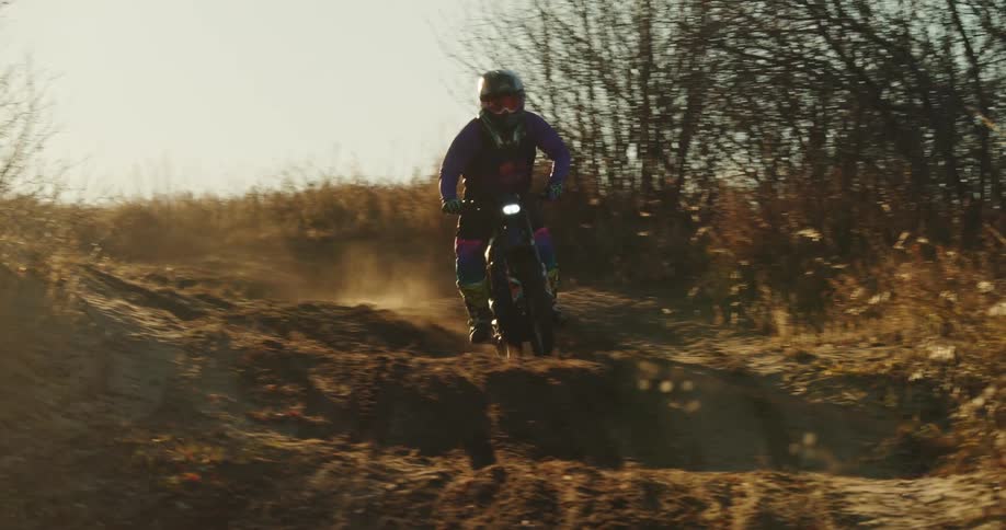 A motocross rider wheelies on a dirt bike over a rugged trail in a sunlit outdoor setting