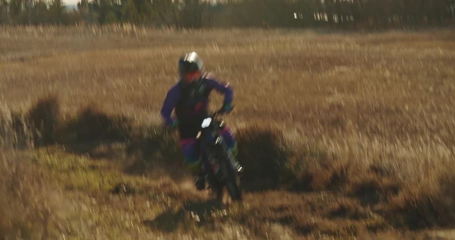 A motocross rider speeds through a dry grassy field wearing colorful gear and a helmet