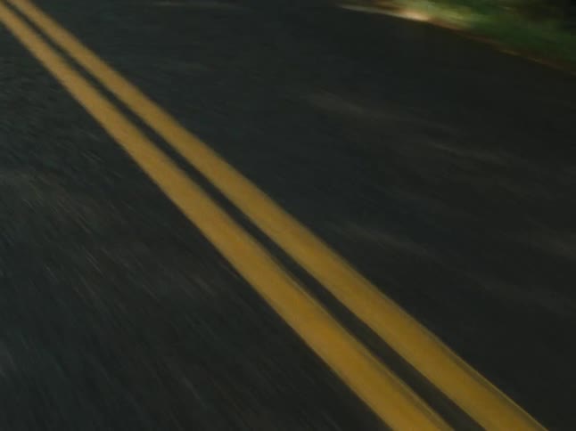 A lowangle shot captures the perspective of driving on an asphalt road with clear double yellow lines and motion blur on the sides