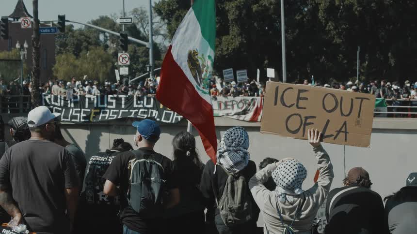 La protesters stand with signs and a mexican flag while protesting the ice raids