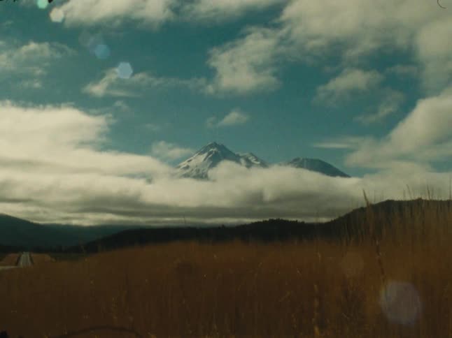 Snowcapped mountain rises through a dramatic sky above golden grasslands