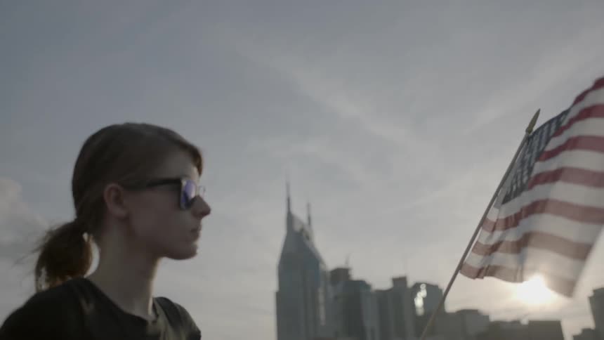 A woman holds an american flag with city buildings in the background