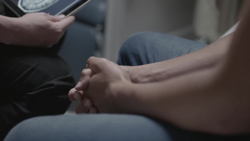 A person sitting opposite another clasps his hands together