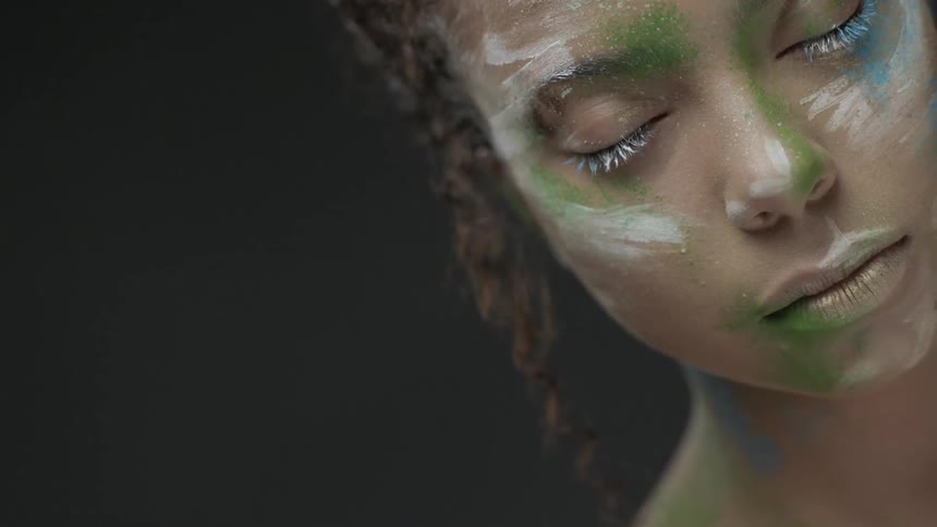 A woman with face paint opens her eyes