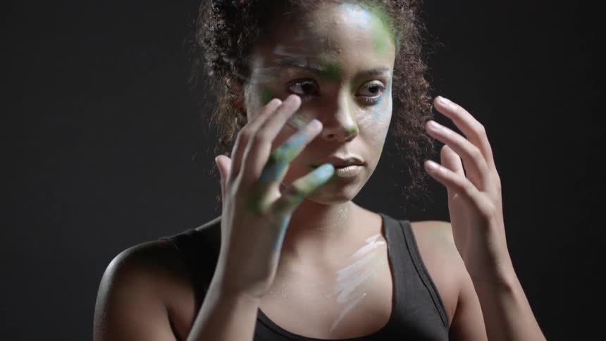A woman with face paint holds her hands up near her face