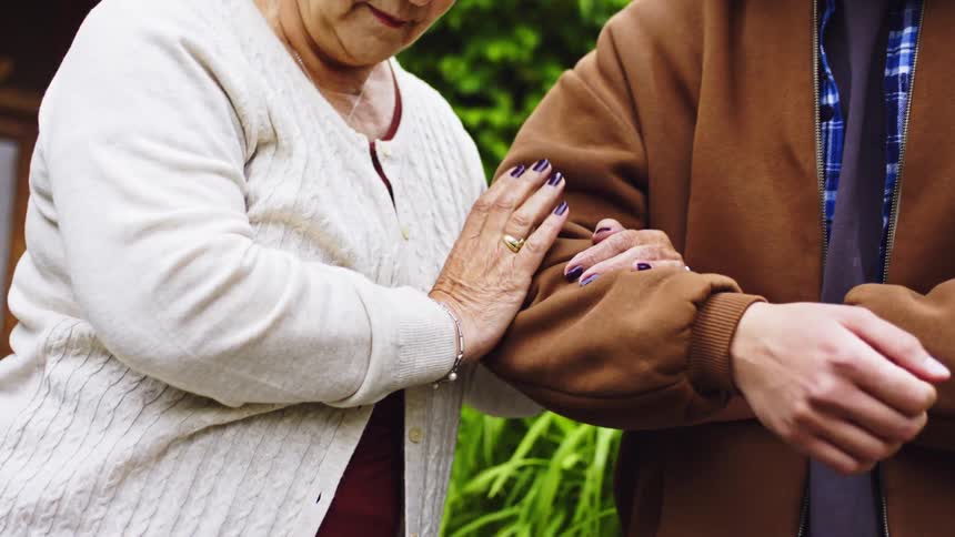 Male teen helps an elderly woman walk down a flight of stairs at the entrance of a home during daytime