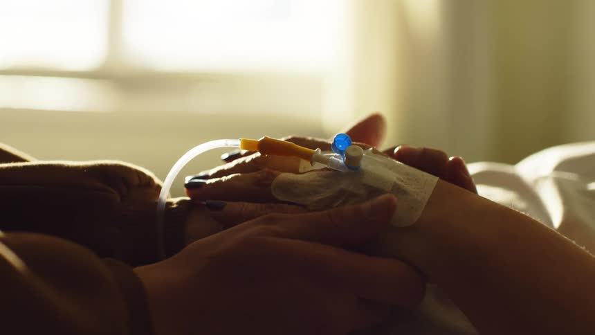 A visitor is holding the hand of a hospital patient