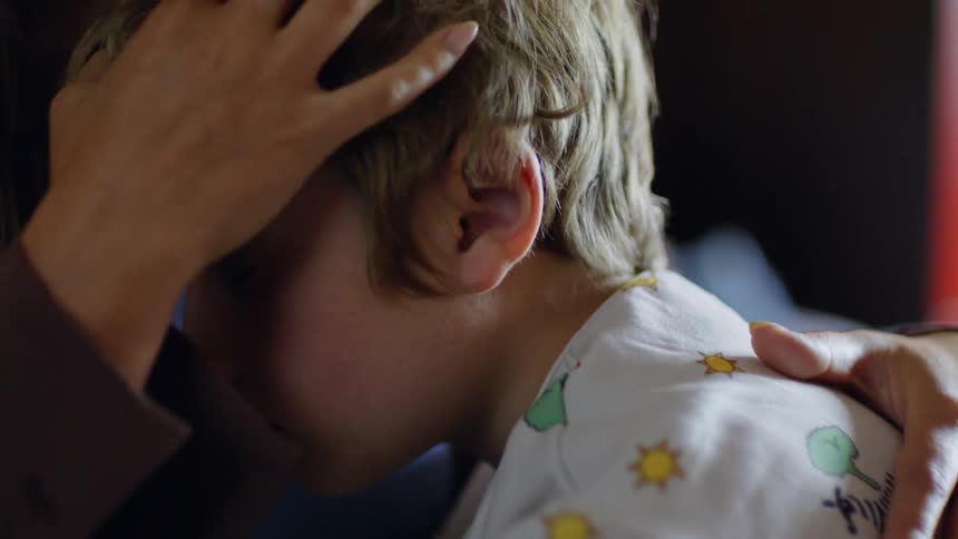 Mother caresses son as her sleeps on her chest in a room