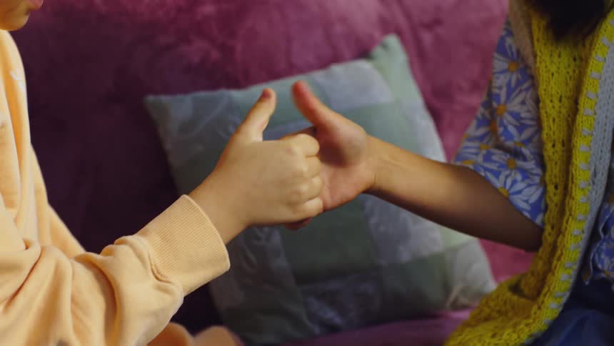 Close up of a boy and girl holding hands while playing a thumb battle game