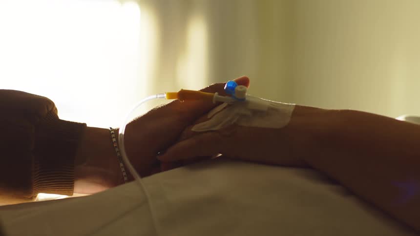 A hospital patient holds hands with a visitor