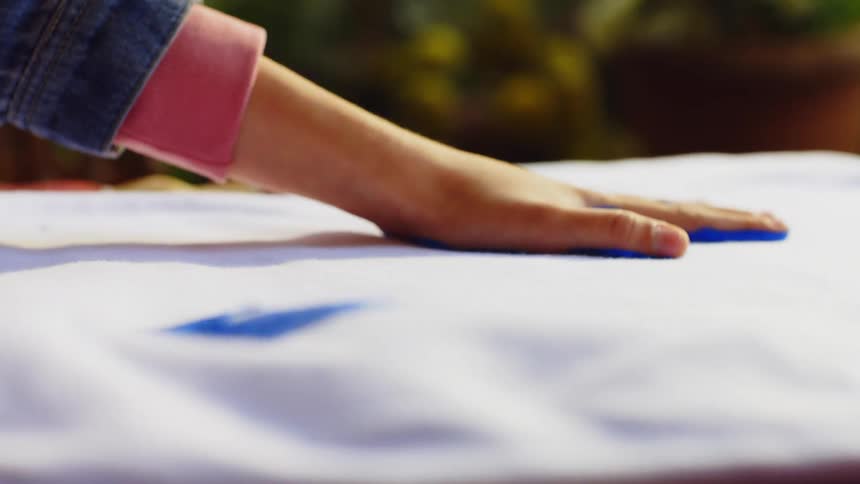 Pair of hands with blue paint being placed on a white tshirt