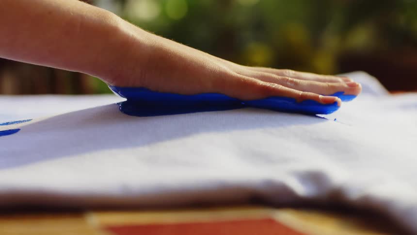 Close up of a person placing blue hand paint prints on a white piece of clothing