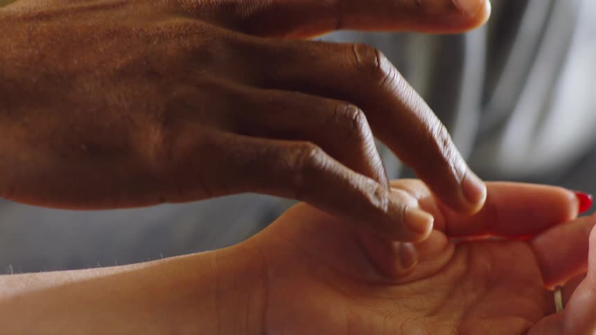 Fingers of one person touching the arm of another person who holds their hands together