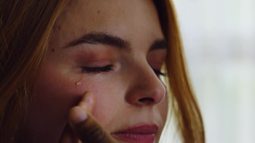 A tearful woman with closed eyes is gently comforted by a hand on her face