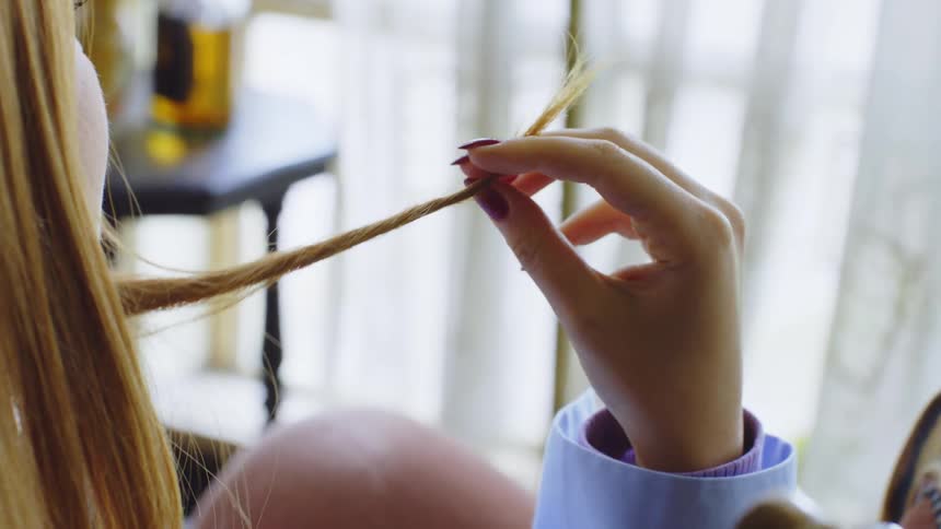 Close up of a blonde girl twisting her hair while sitting in a room