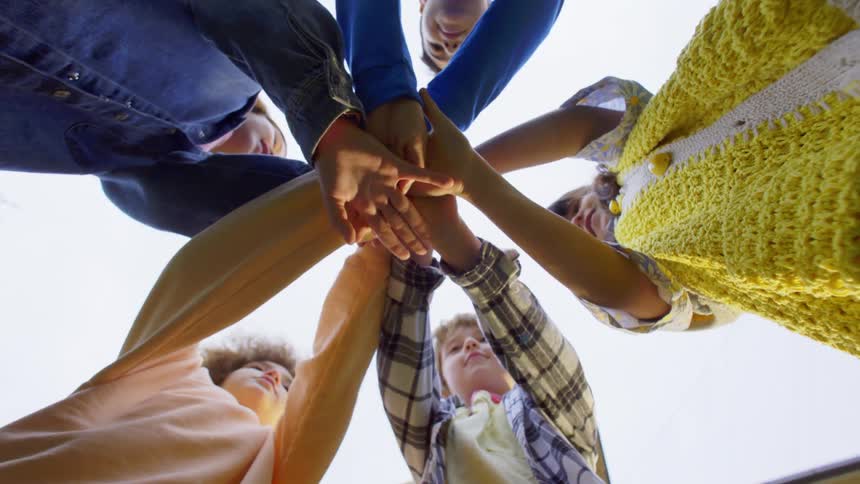 Group of children placing their hands on top of each other and cheering with joy