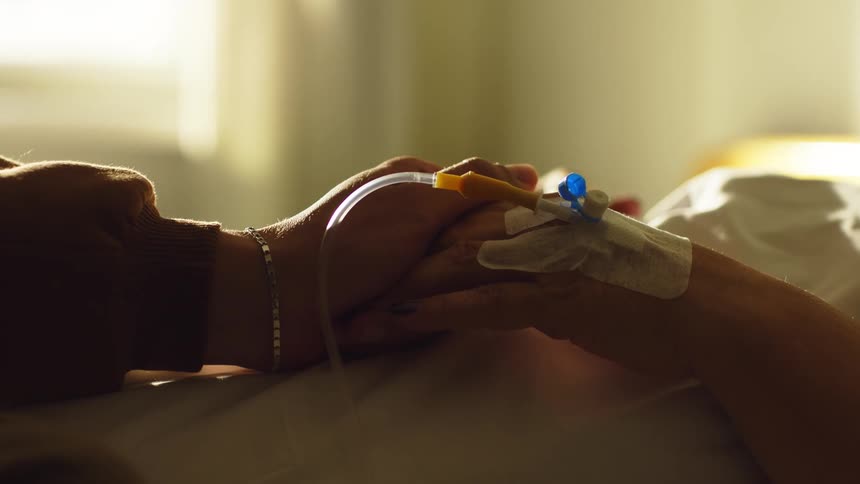 Two hands clasped together as a person lies on a hospital gurney
