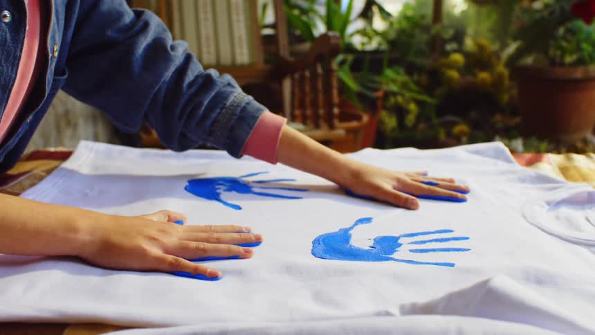 A woman is putting hand prints of blue paint on a shirt