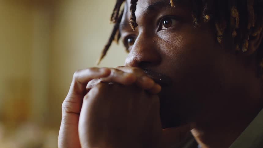 Closeup of a man resting his face on his clasped hands gazing thoughtfully into the distance