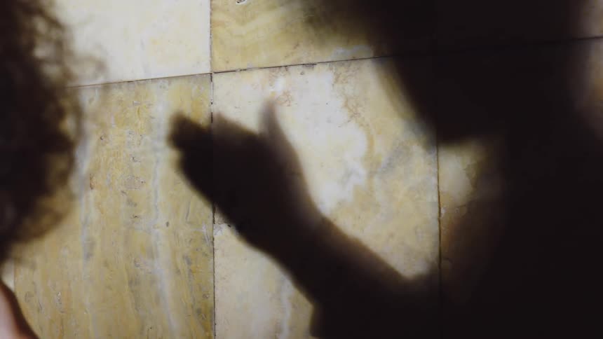Person making hand gestures with their shadow reflecting on the wall