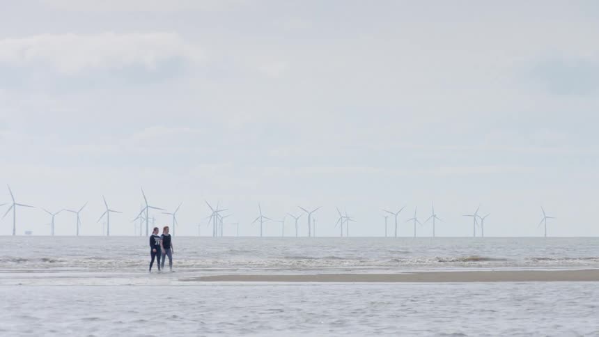 Two people walk along the beach on a cloudy day