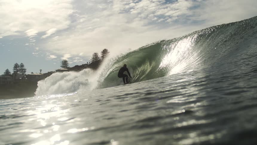 A person surfs beneath a massive wave forming in the ocean at midday
