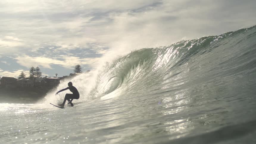 A person is surfing a breaking wave on a clear day with sun reflections on the surface of the water