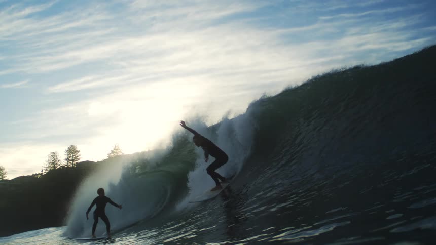 Man and woman riding the sea wave at sunset
