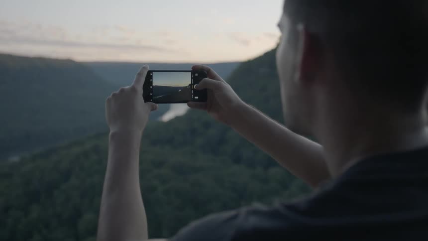 A man takes a picture of a wooded valley