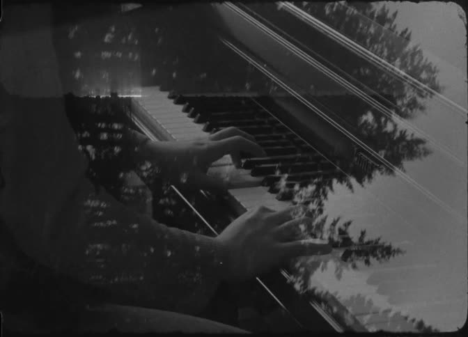 A persons hands playing the keys of a piano and a light of silhouettes of trees passing in front