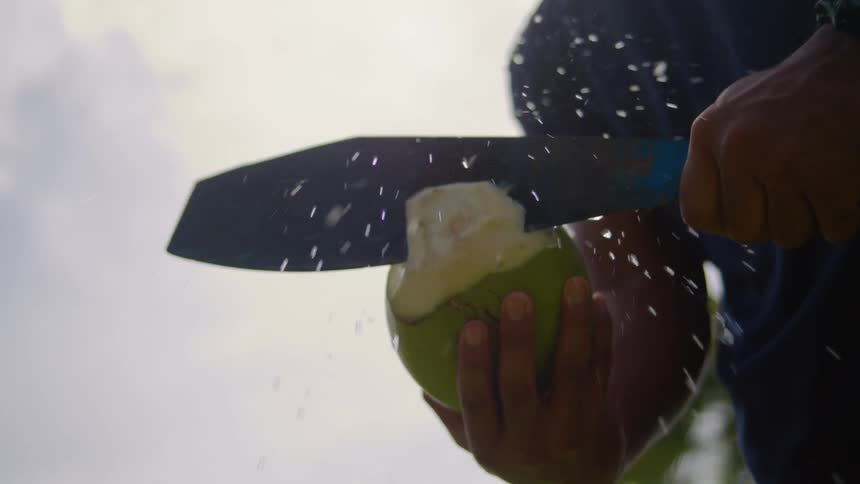 Close up of a black male cutting a coconut open with a blade outdoors