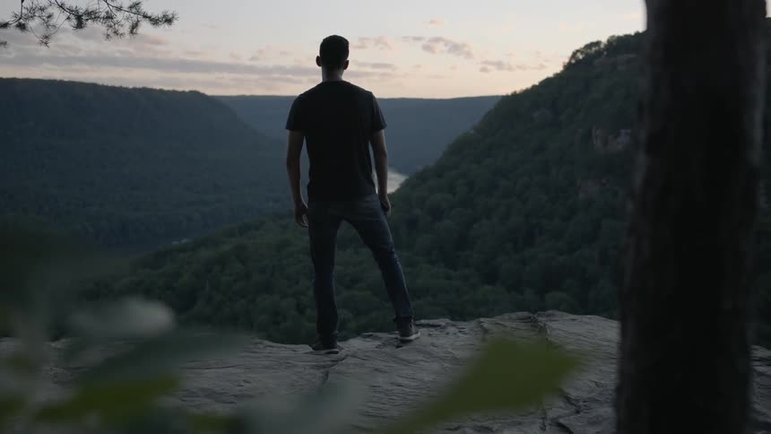 A man looks out at a valley at sunset