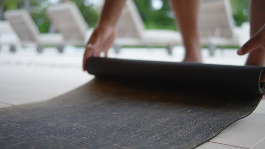 Man rolling out yoga mat on tile flooring outdoors in tropical location