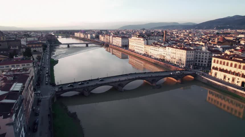Vehicles cross a river bridge in the residential area of a city bordering the mountains