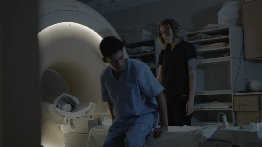 Man shakes woman's hand then lays down on a medical machine