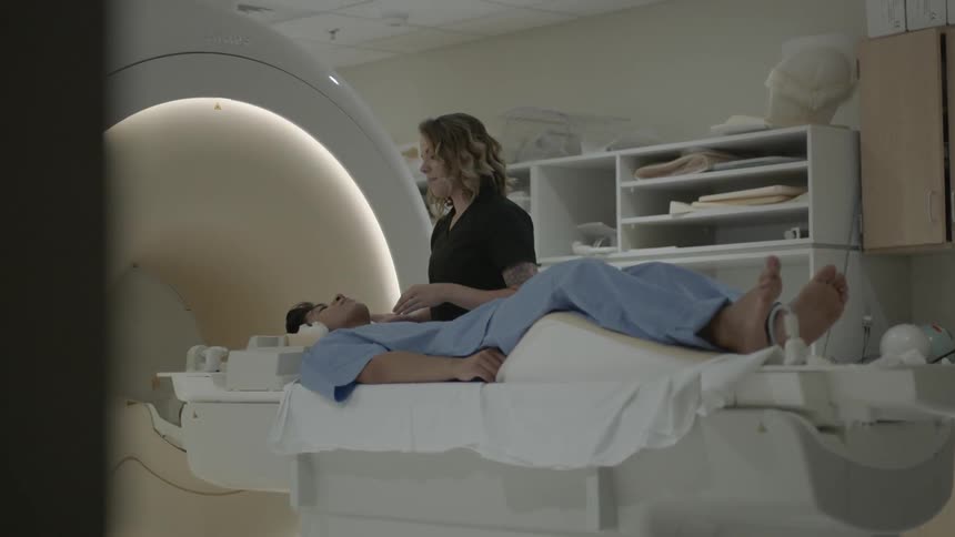 Woman puts headphones on man's head to prepare for mri