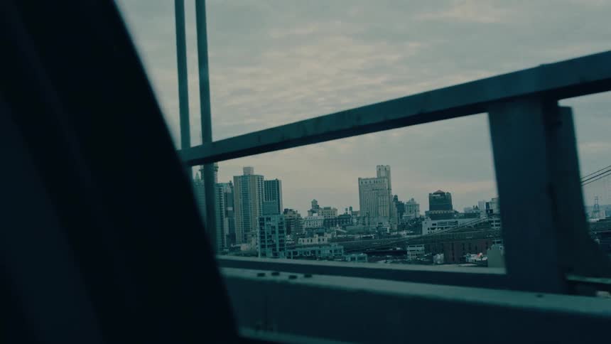 A car drives across a bridge at sunrise with the city skyline visible through the window