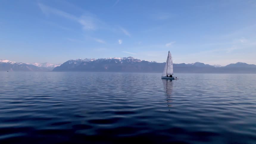 A lone sailboat drifts peacefully on a vast calm lake surrounded by distant mountain ranges