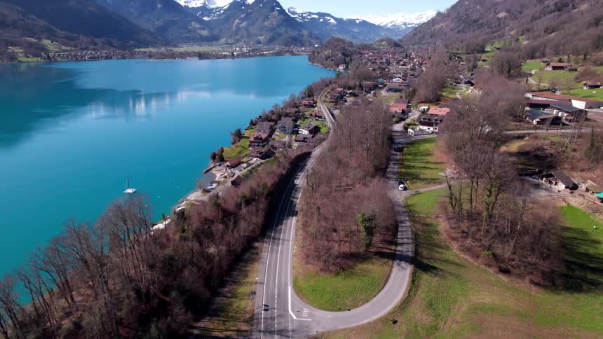 A serene lakeside village sits at the base of snowcapped mountains under a clear blue sky