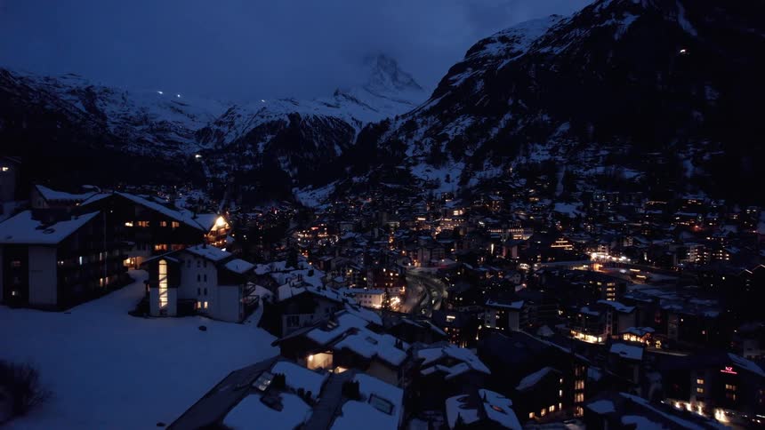 Yellow lights from windows light up a snow covered city in the mountains at night