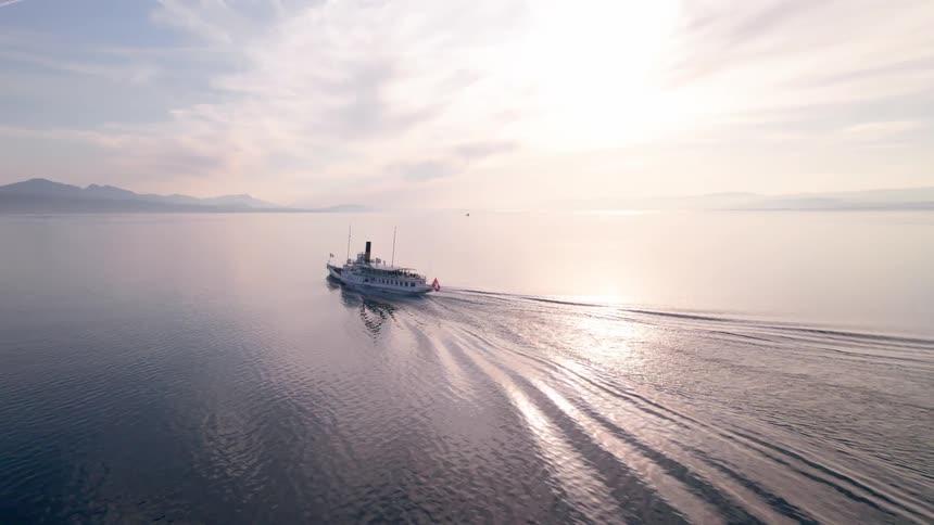 A big white boat sailing on a sea of calm water with mountains in the background and the sky with white clouds