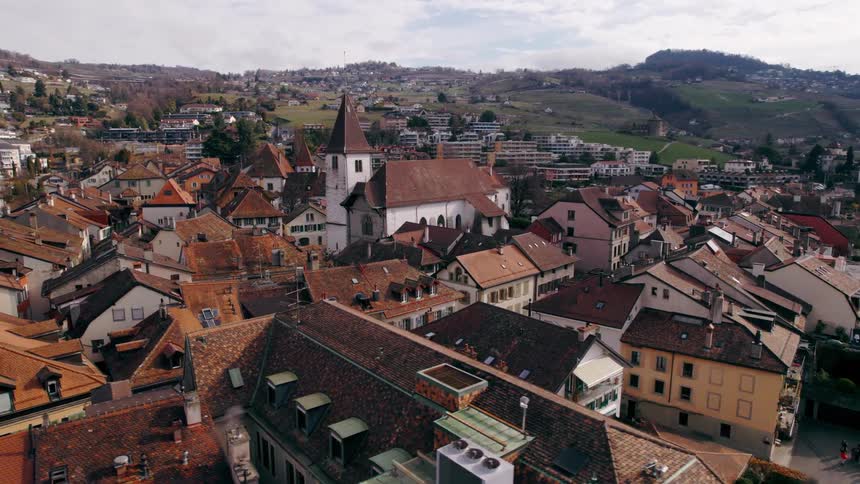 A scenic aerial view of a european village with a prominent church steeple nestled by a lake and hillside