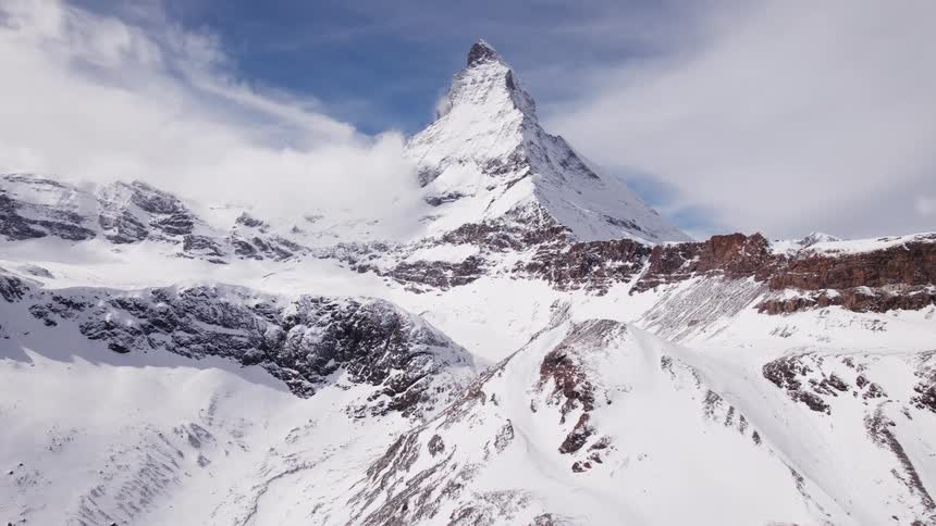 An epic aerial view reveals the iconic snowcovered peak of the matterhorn mountain rising dramatically above a vast snowy mountain range and clouds
