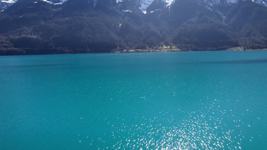 A large mountain range is on the shore with blue water