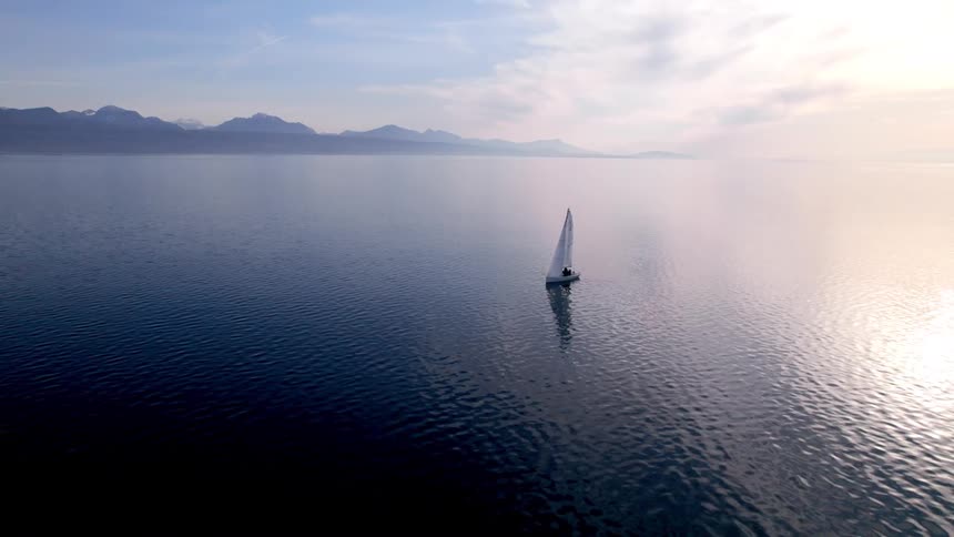A sailboat sailing on a large body of calm water on a clear day with sunlight reflecting off the surface