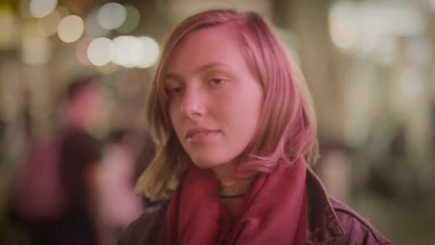 A young woman stands under city lights at night looking calmly ahead