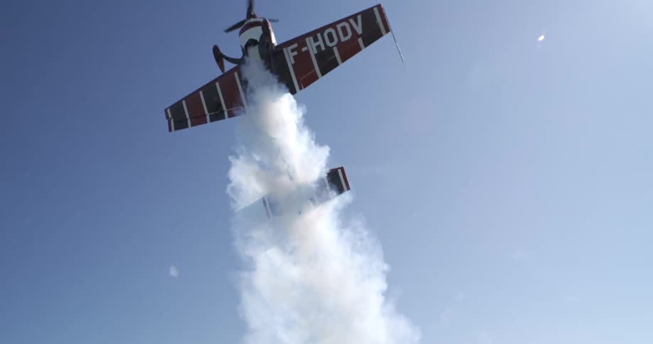 A stunt plane ascends vertically with smoke trailing behind against a clear blue sky